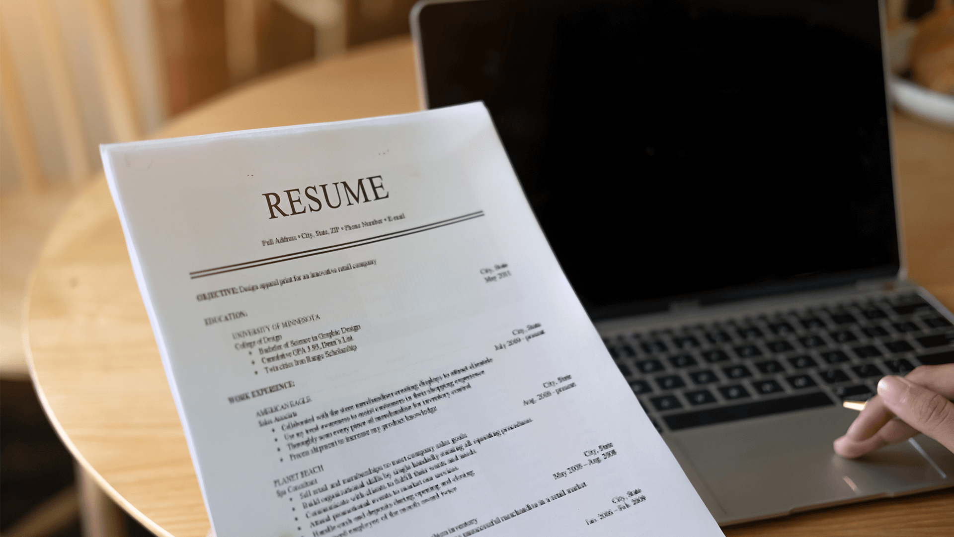 Prepping for success: a job seeker reviews their resume before sending off their application, with their trusty laptop at the ready for final edits and online submissions.