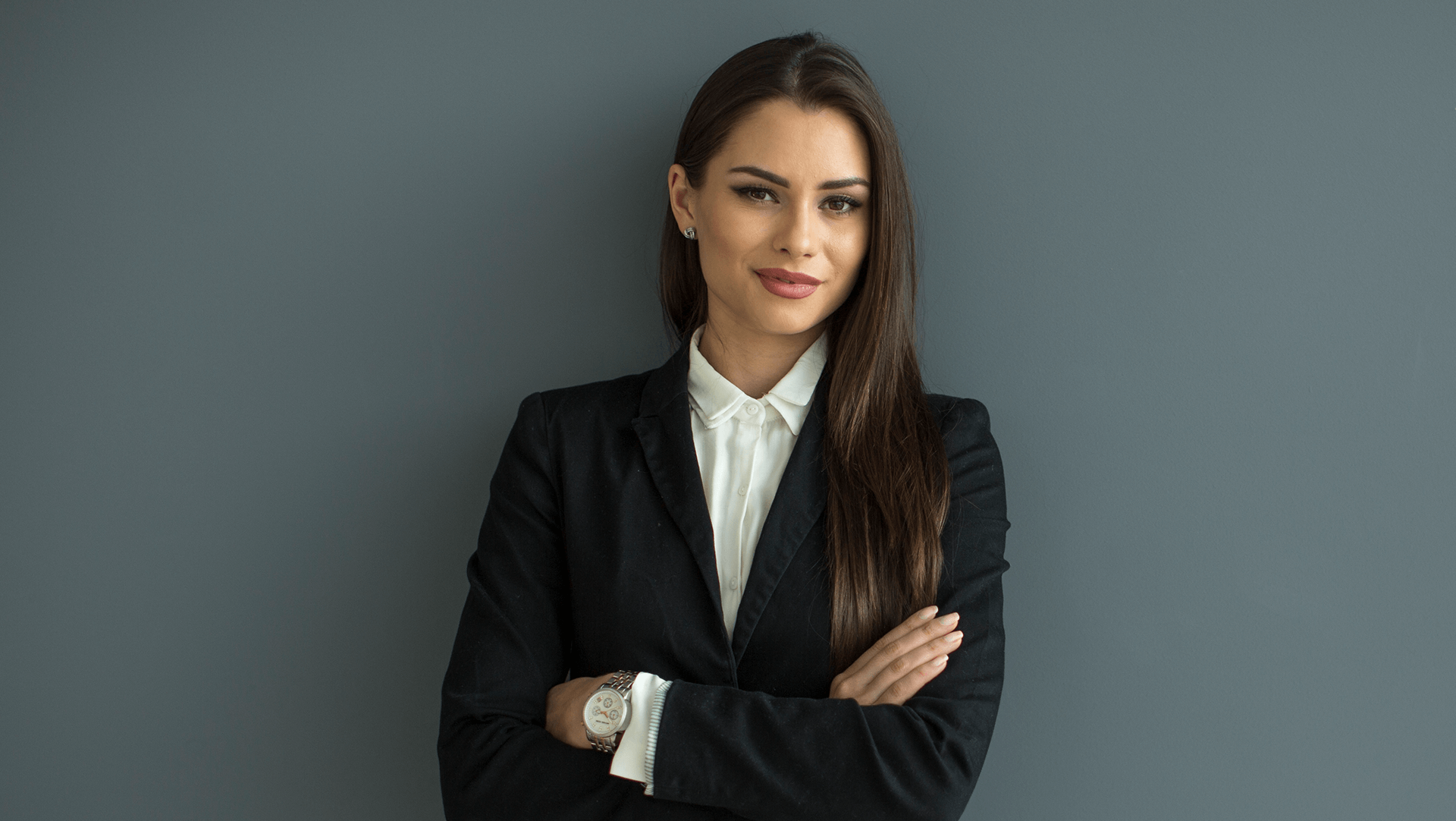 Confident professional woman with crossed arms standing against a gray background.