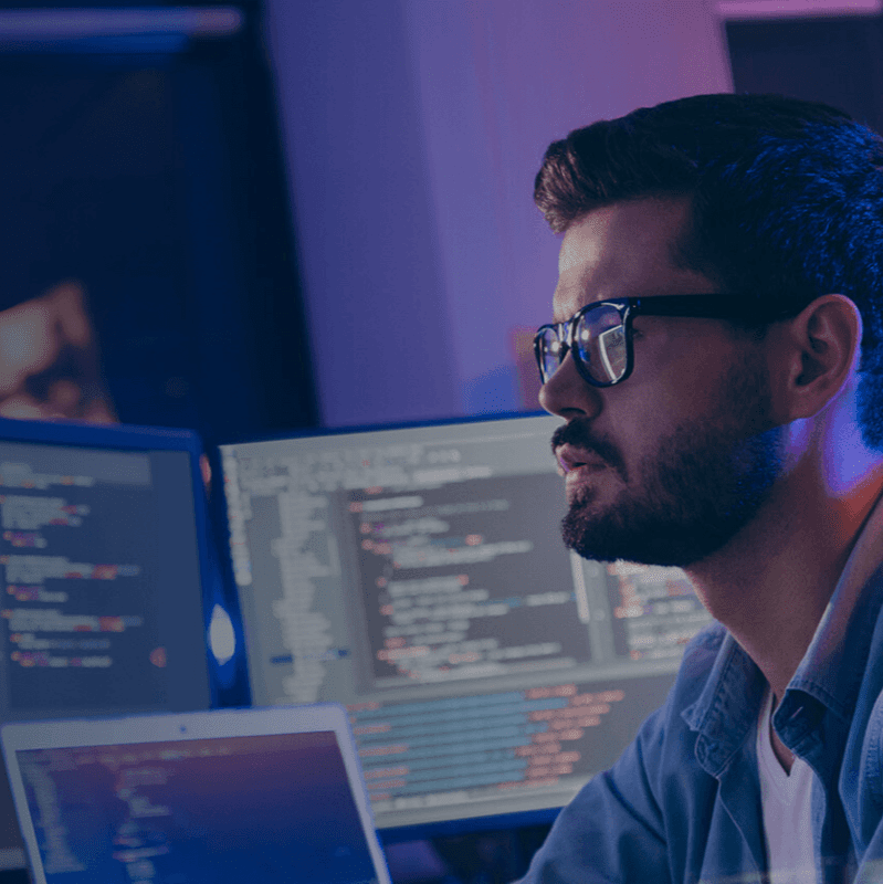 Focused software developer working late, engrossed in coding on multiple computer screens.