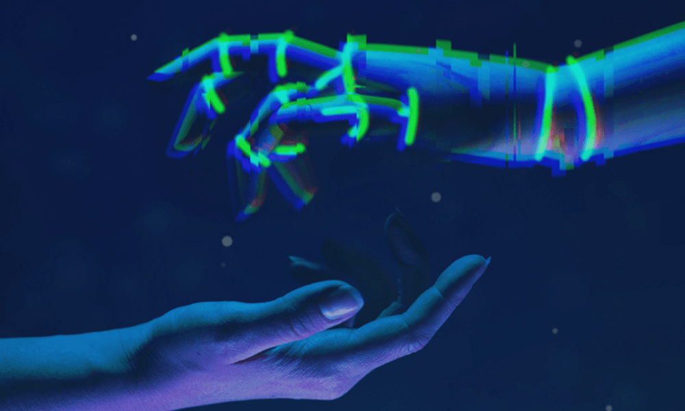 A human hand reaches out to a digital, pixelated hand under a dark blue background with small stars. The digital hand appears in glowing shades of blue and purple, creating a contrast with the natural skin tone of the human hand.