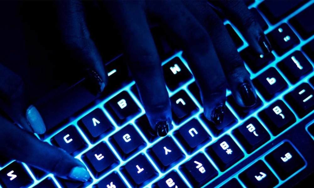 Hands typing on a backlit keyboard in a dimly lit environment, highlighting the interplay of technology and user interaction.